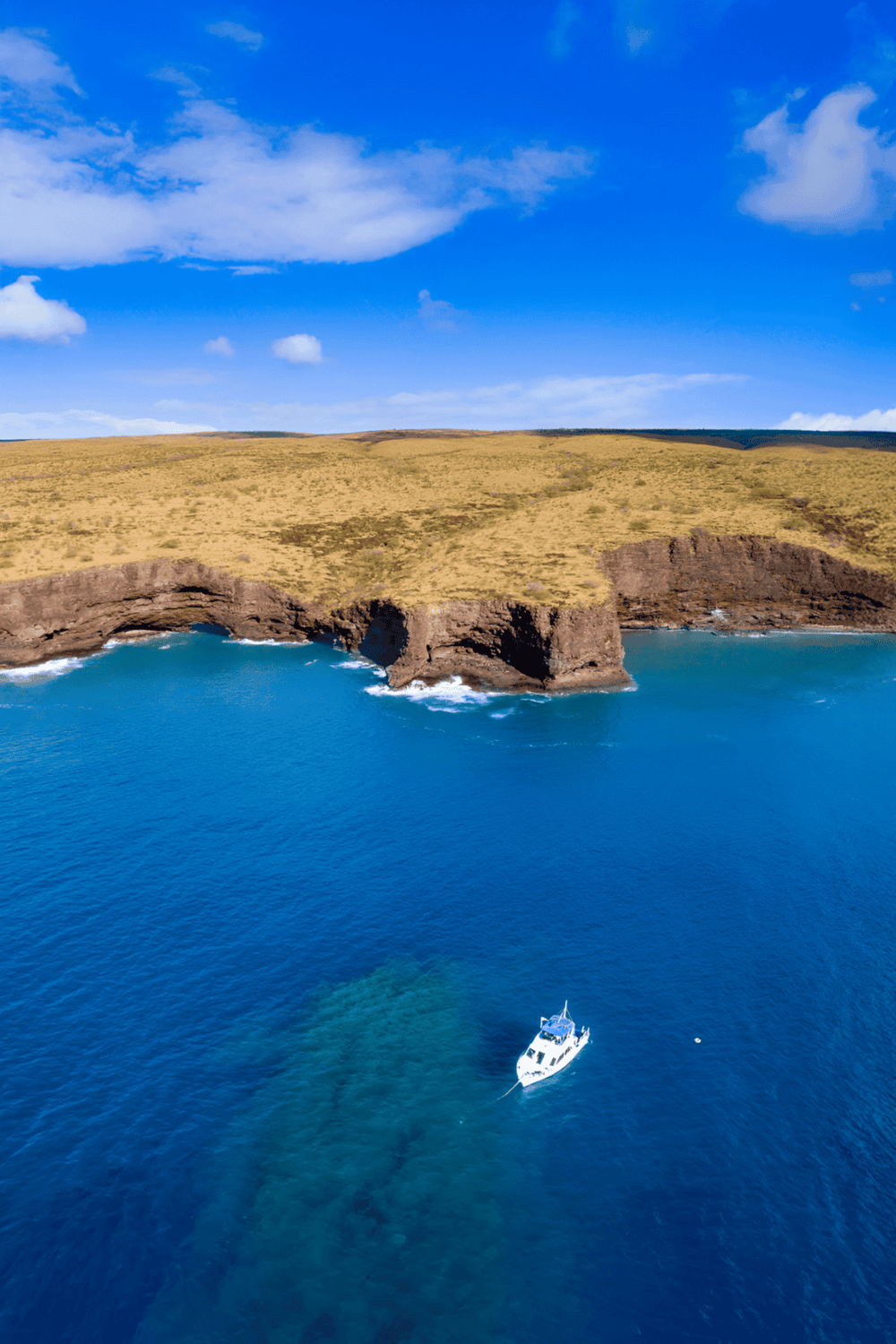 Secluded coastal cliffs with a rock arch, blue ocean, and boat, emphasizing adventure and exploration.