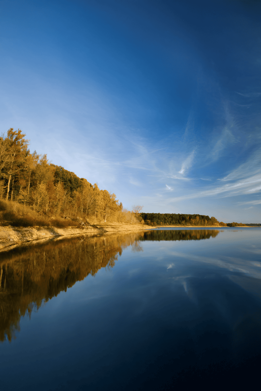 Tranquil lakeside landscape with autumn trees under a clear blue sky, perfect for outdoor adventure and nature exploration.