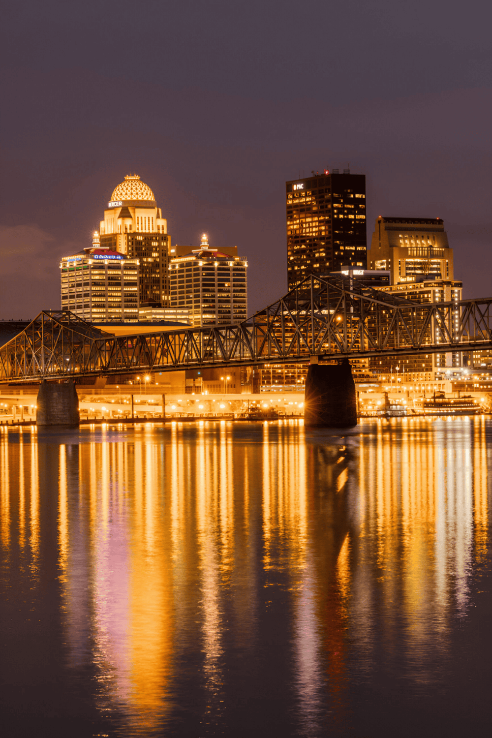 Downtown Indianapolis skyline at night with illuminated buildings and reflections on the water.