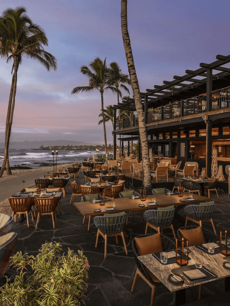 Relaxing beachfront restaurant with ocean view and palm trees at sunset.