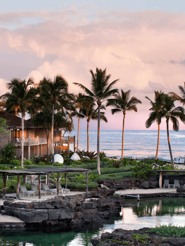 Palm trees over beachfront resort with ocean view and pool, tropical vacation destination.