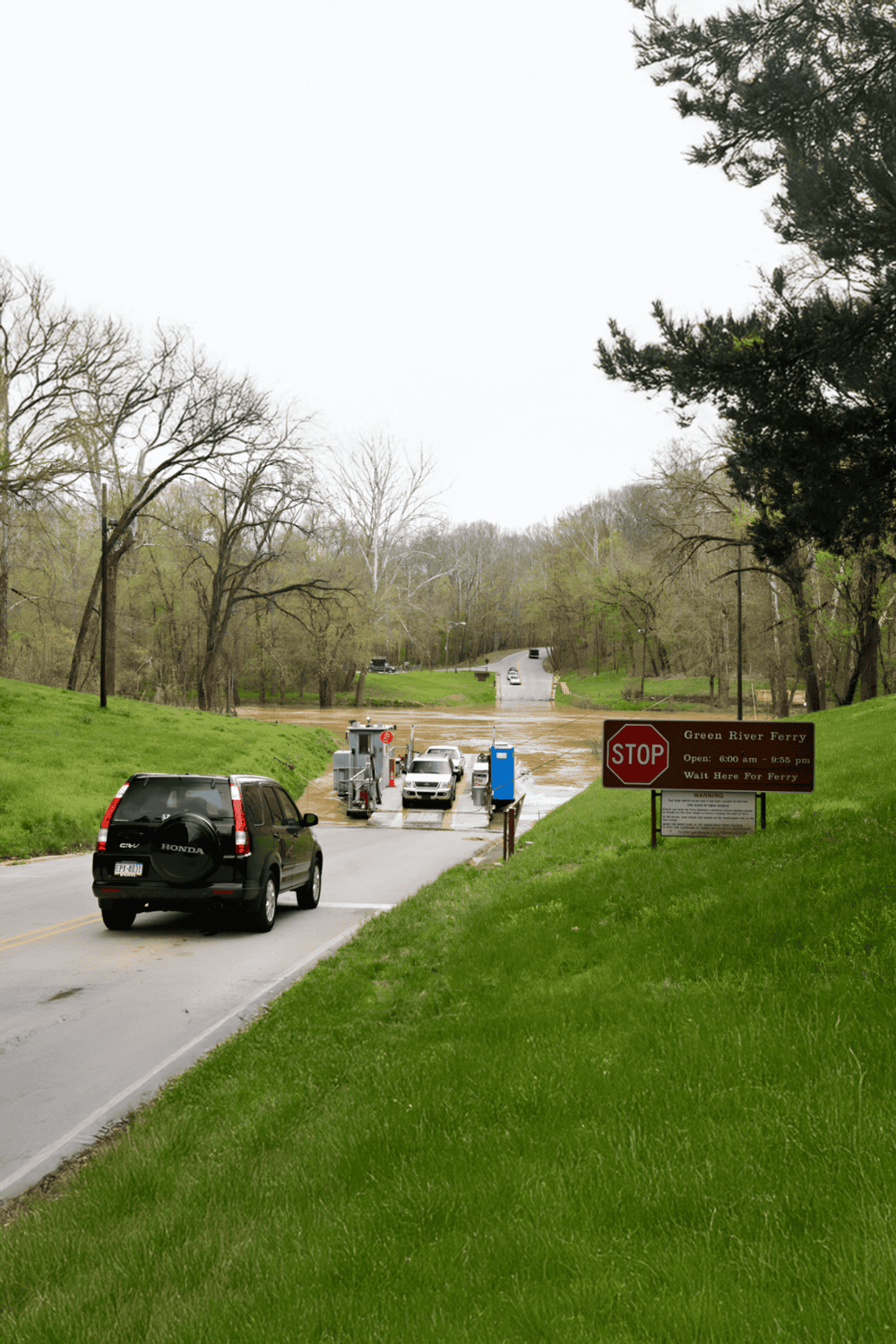 Ferry crossing at Green River with cars boarding the boat, surrounded by green trees and a stop sign.