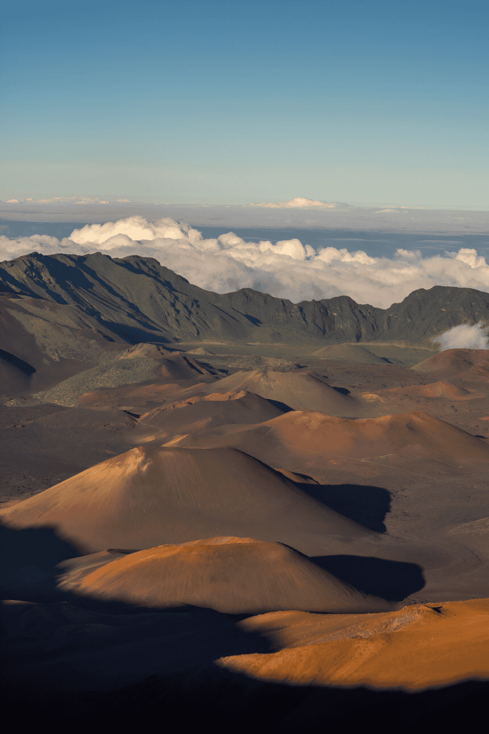 Volcanic landscape with colorful cinder cones, mountain range, and sky in the background.
