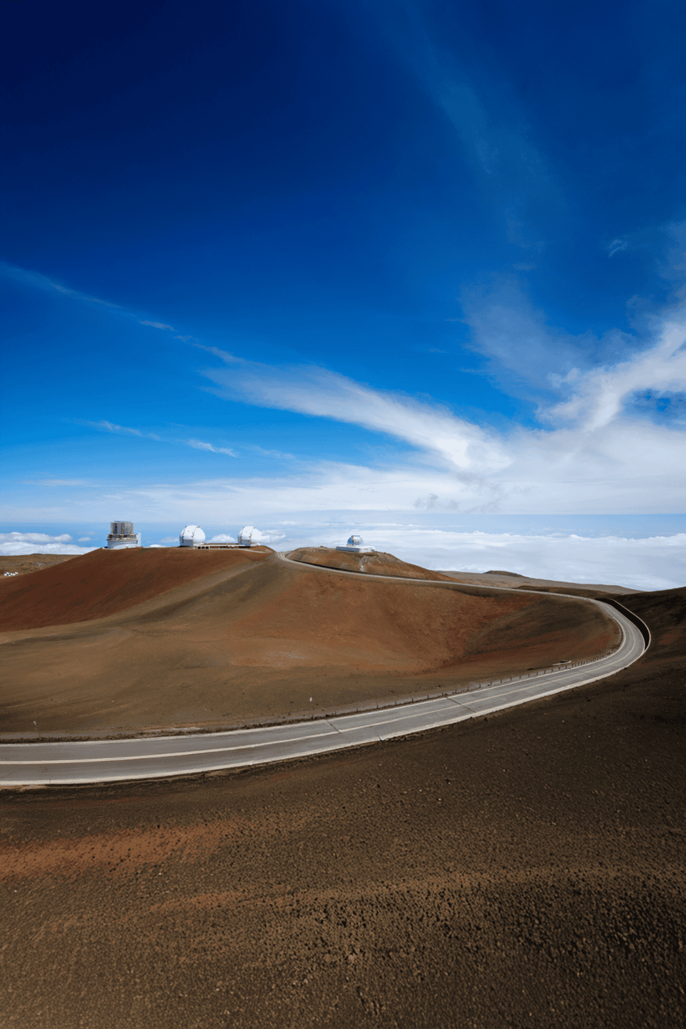 Himalayan mountain landscape with observatories and a winding road, under a bright blue sky.