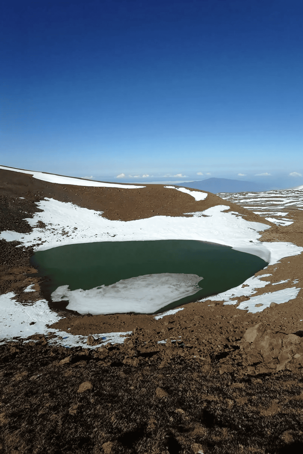 Snow-capped mountain landscape with a small green pond in the wilderness.