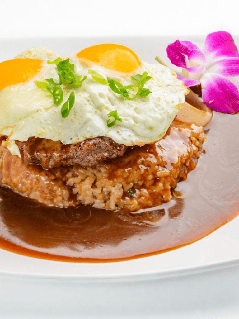 Eggs Benedict with steak, rice, and rich sauce garnished with green onions and a purple orchid.