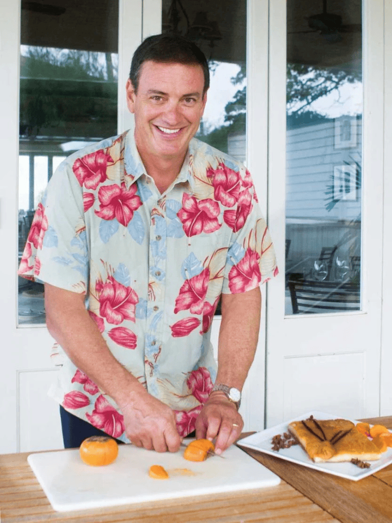 1. Relaxed man in colorful Hawaiian shirt preparing food for outdoor gathering.
