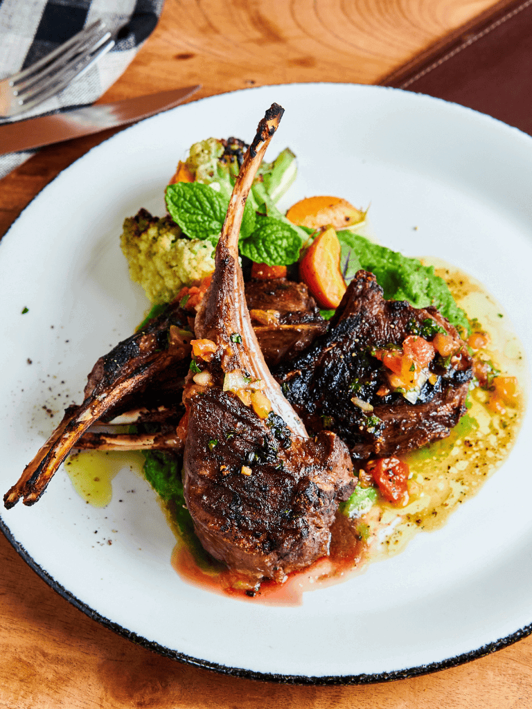 Succulent grilled lamb chops with vibrant vegetable garnish and fresh herbs on a white plate.