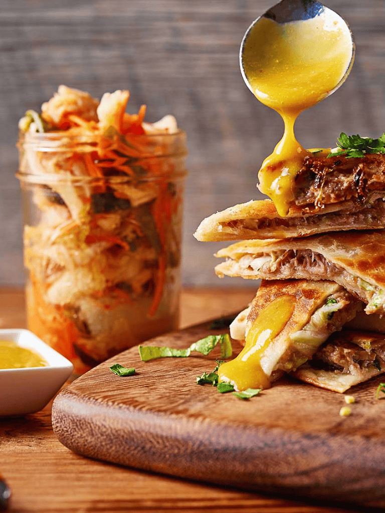 Savory meat-filled quesadilla with melted cheese, served with dipping sauce on wooden board.