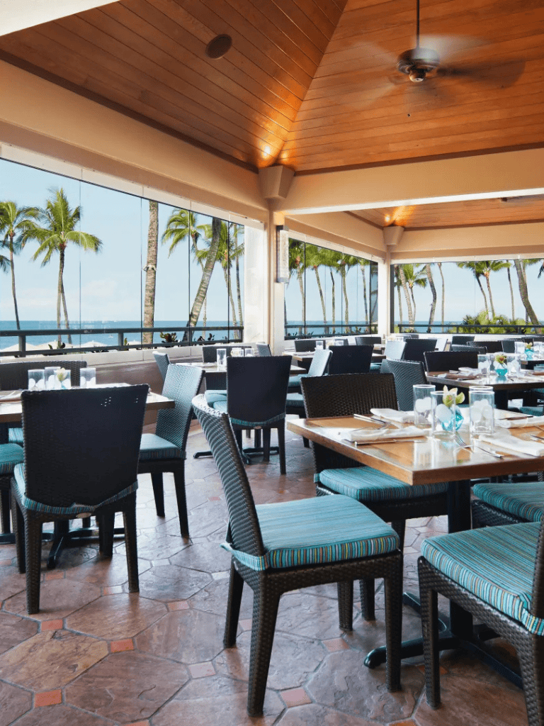 A tropical restaurant with ocean view, palm trees, and elegant dining setup, perfect for seaside dining experiences.