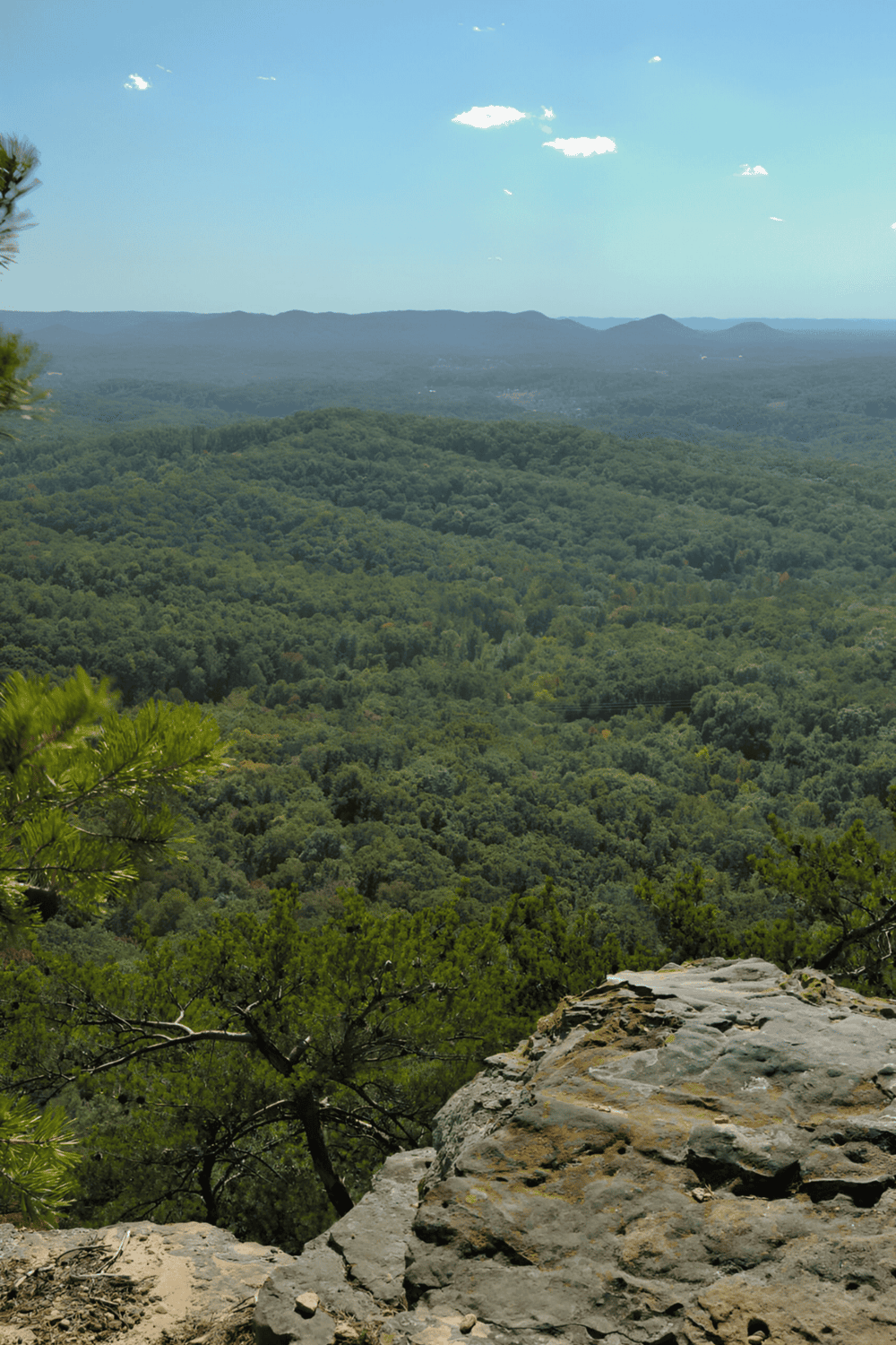 Expansive view of lush green mountains and forested landscape with blue sky and clouds.