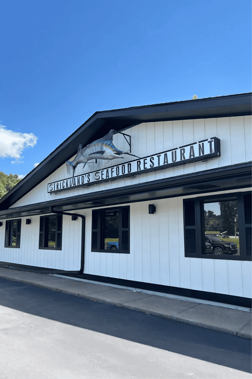 A fish-shaped sign on a seafood restaurant building with blue sky in the background.