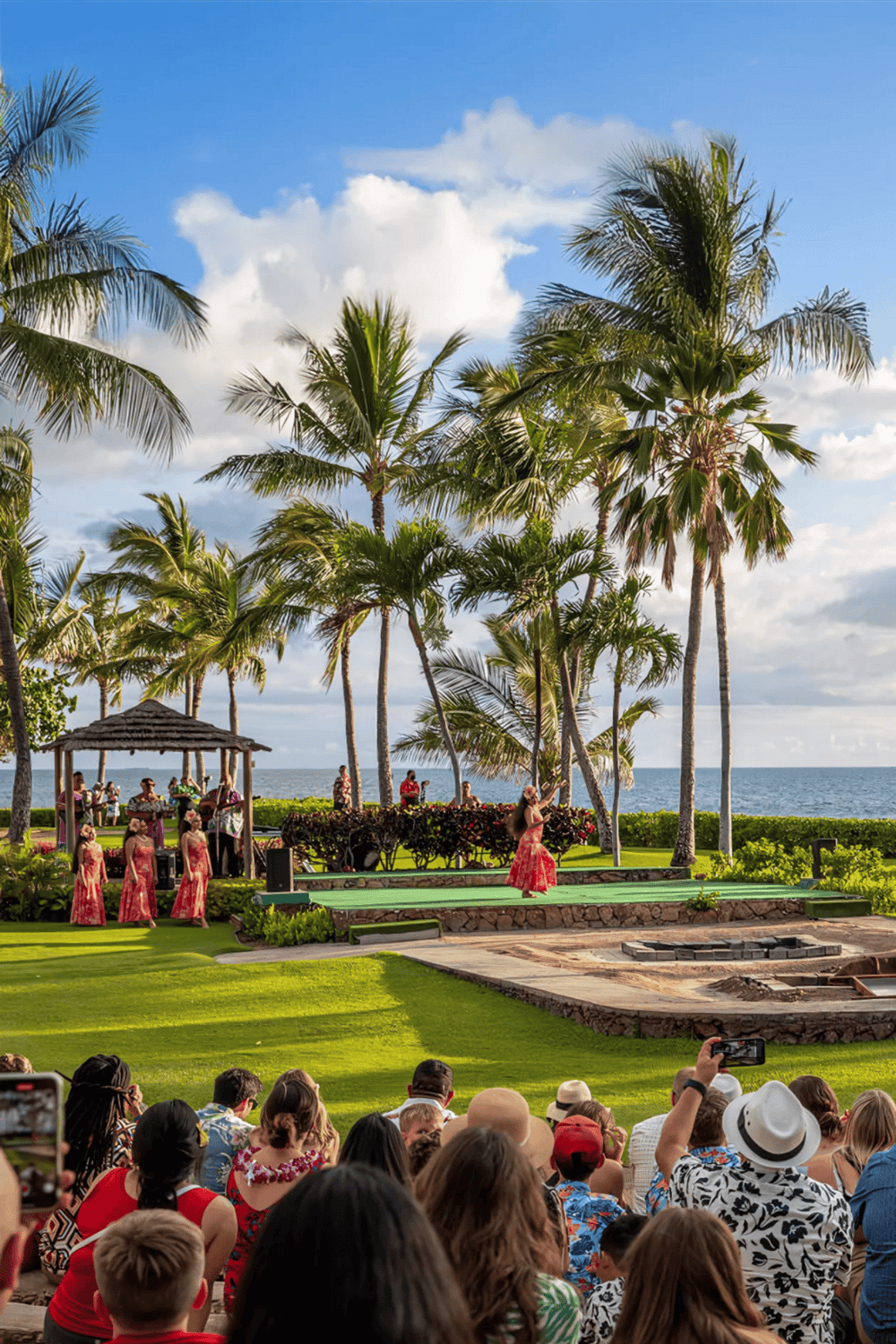 Hawaii outdoor luau performance with dancers, palm trees, ocean view, and audience enjoying cultural entertainment.