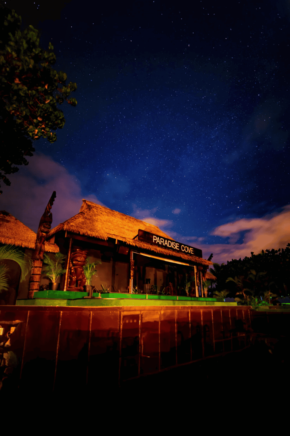 Night sky with stars over Paradise Cove, tropical beachfront bar and restaurant at dusk.