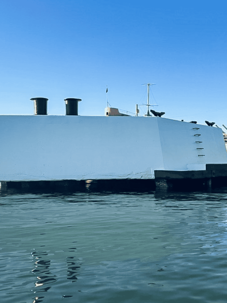 Vintage warship anchored on calm water with clear blue sky background.
