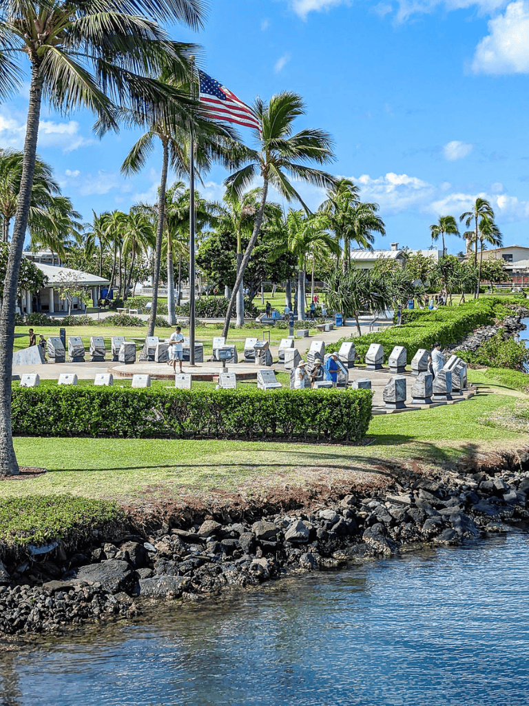 American flag flying at a memorial surrounded by palm trees in a tropical park, sunny weather.