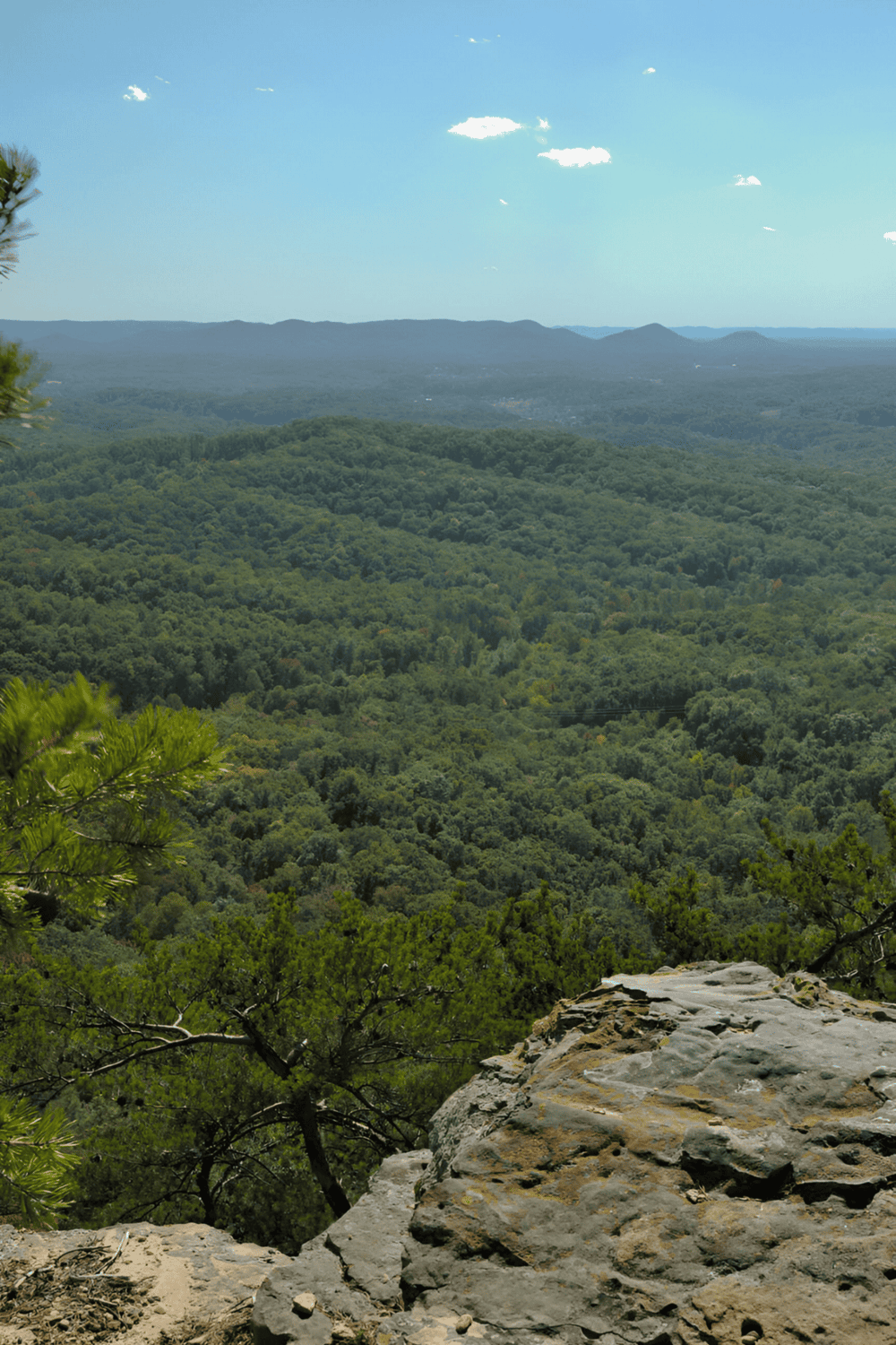 Vast mountain landscape with lush green forests and clear blue sky, scenic view from a hiking trail at QuestForDirections.