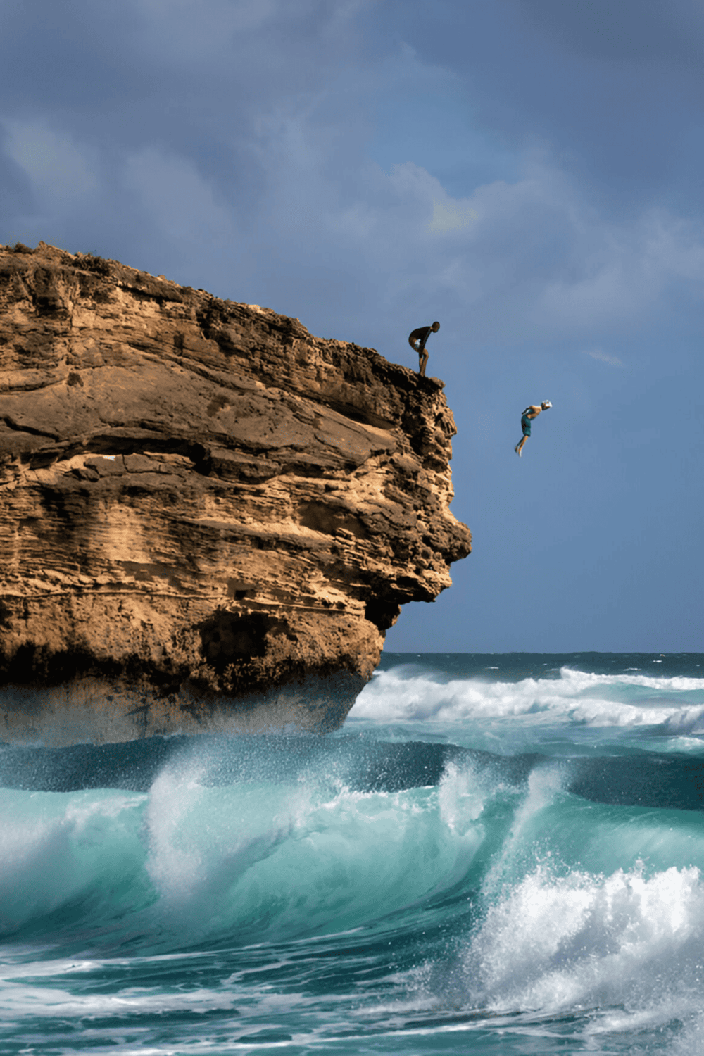1. People jumping off a rocky cliff into ocean waves for adventure and thrill seeking.