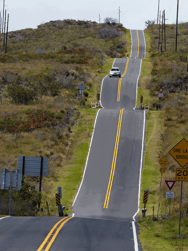 1. Winding rural road with bridge, traffic signs, and hilly landscape.