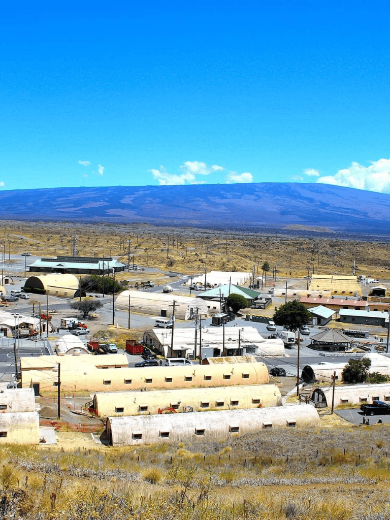 Remote desert town with Quonset hut buildings and volcanic mountain in the background.