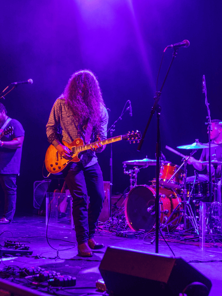 Guitarist performing on stage with vibrant purple lighting at a live music concert.