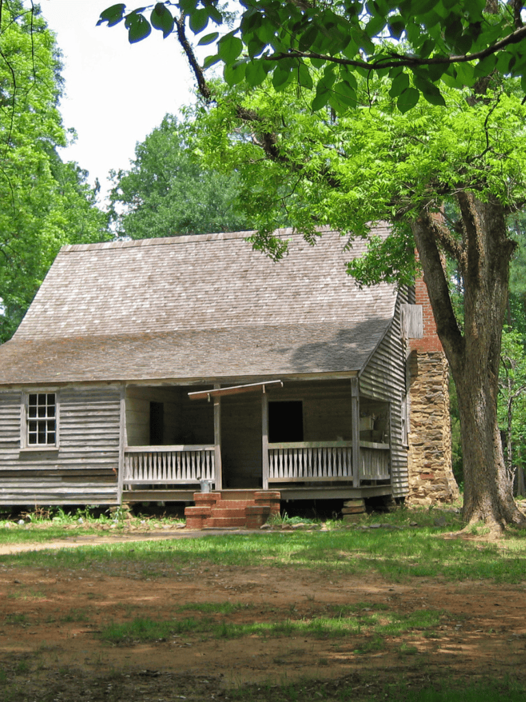 Rustic wooden cabin with porch amidst green trees and nature in the countryside.