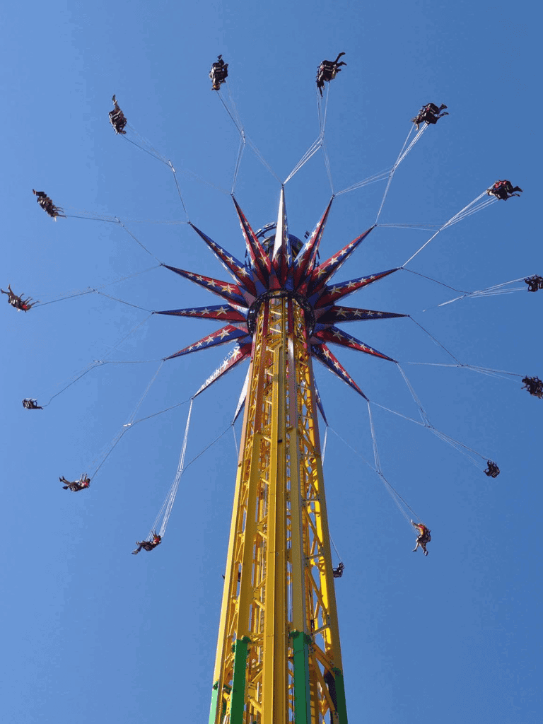 Bright yellow amusement park swing ride with star-spangled decorations against a clear blue sky.
