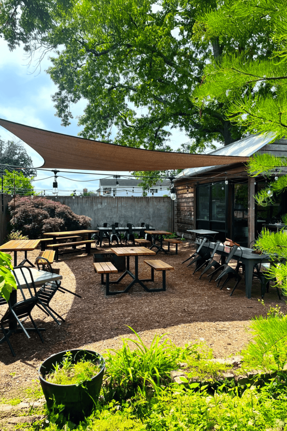 Outdoor dining area with wooden tables and chairs, shaded by a large canopy, perfect for garden restaurant ambiance.