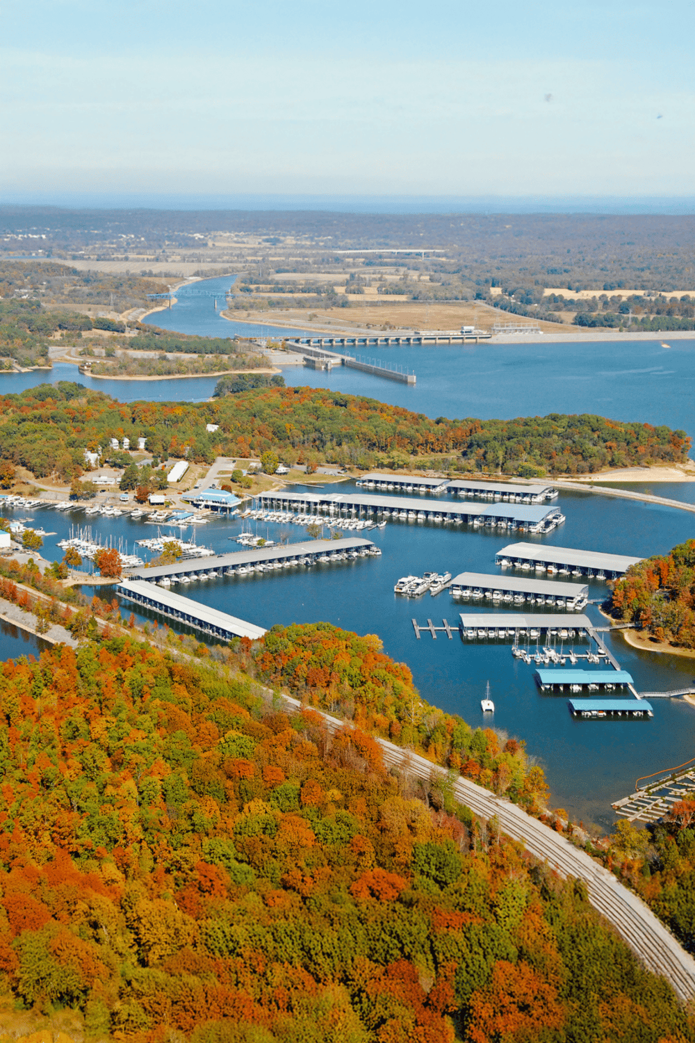 Aerial view of a scenic marina during fall with colorful trees and calm waters.