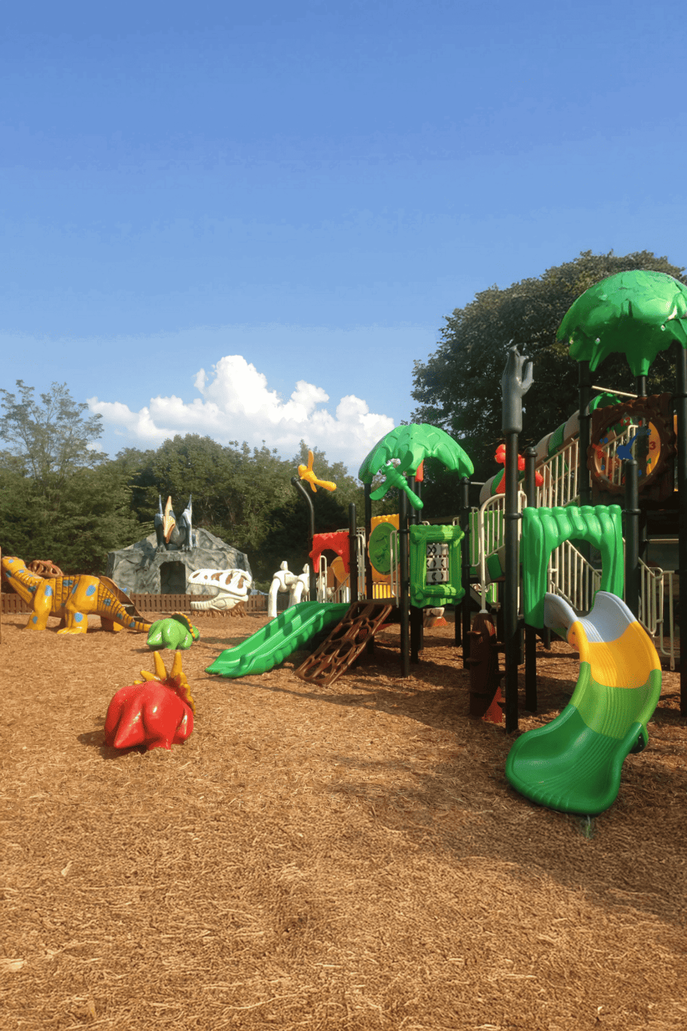 Colorful children's jungle gym with slides and animal sculptures in a park setting.
