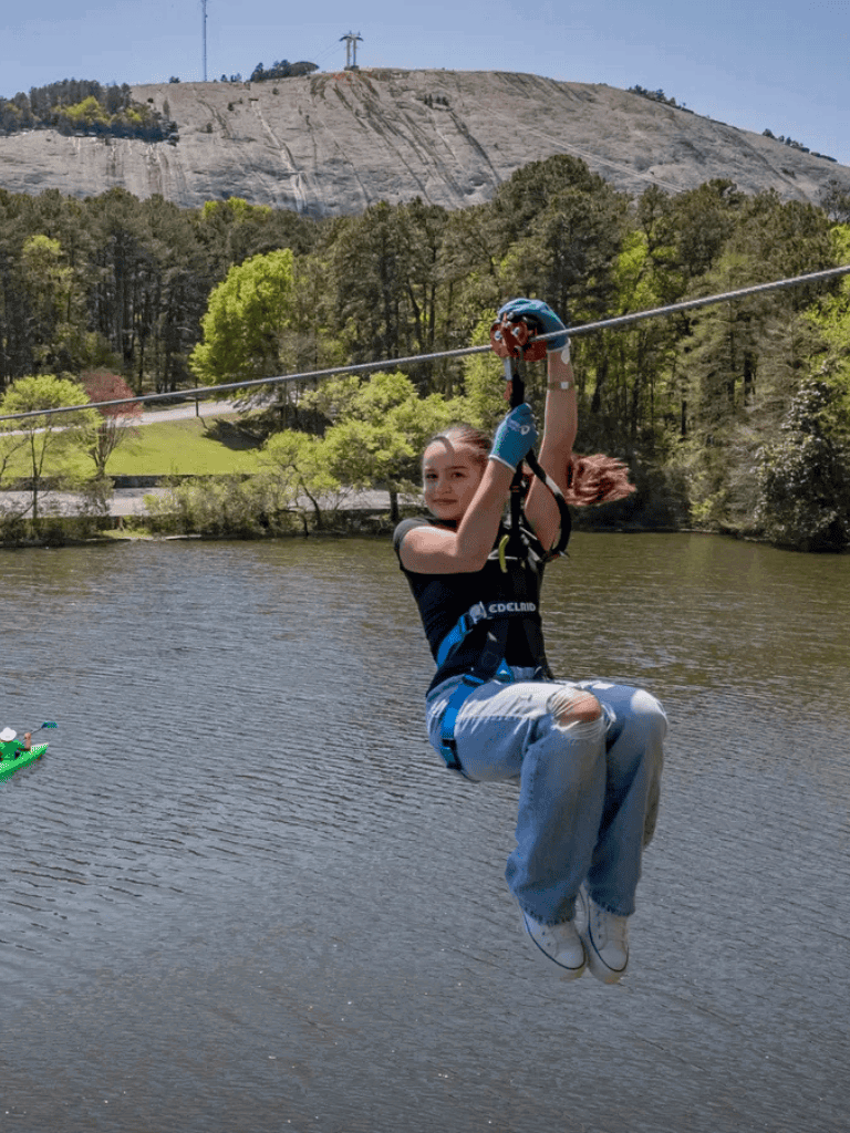 1. Girl ziplining over a lake with lush trees and rocky hills in the background.
