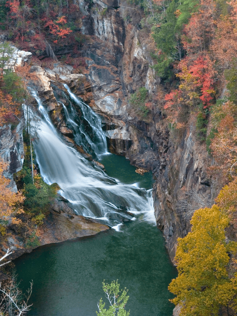 Scenic waterfall in a rocky canyon surrounded by autumn-colored trees.