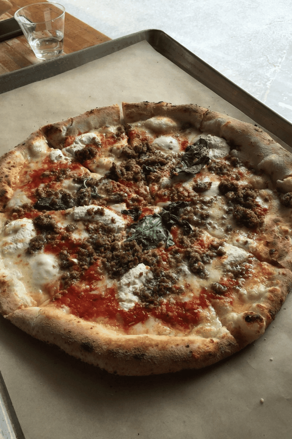 Cheesy sausage pizza with basil on a baking tray at QuestForDirections restaurant.