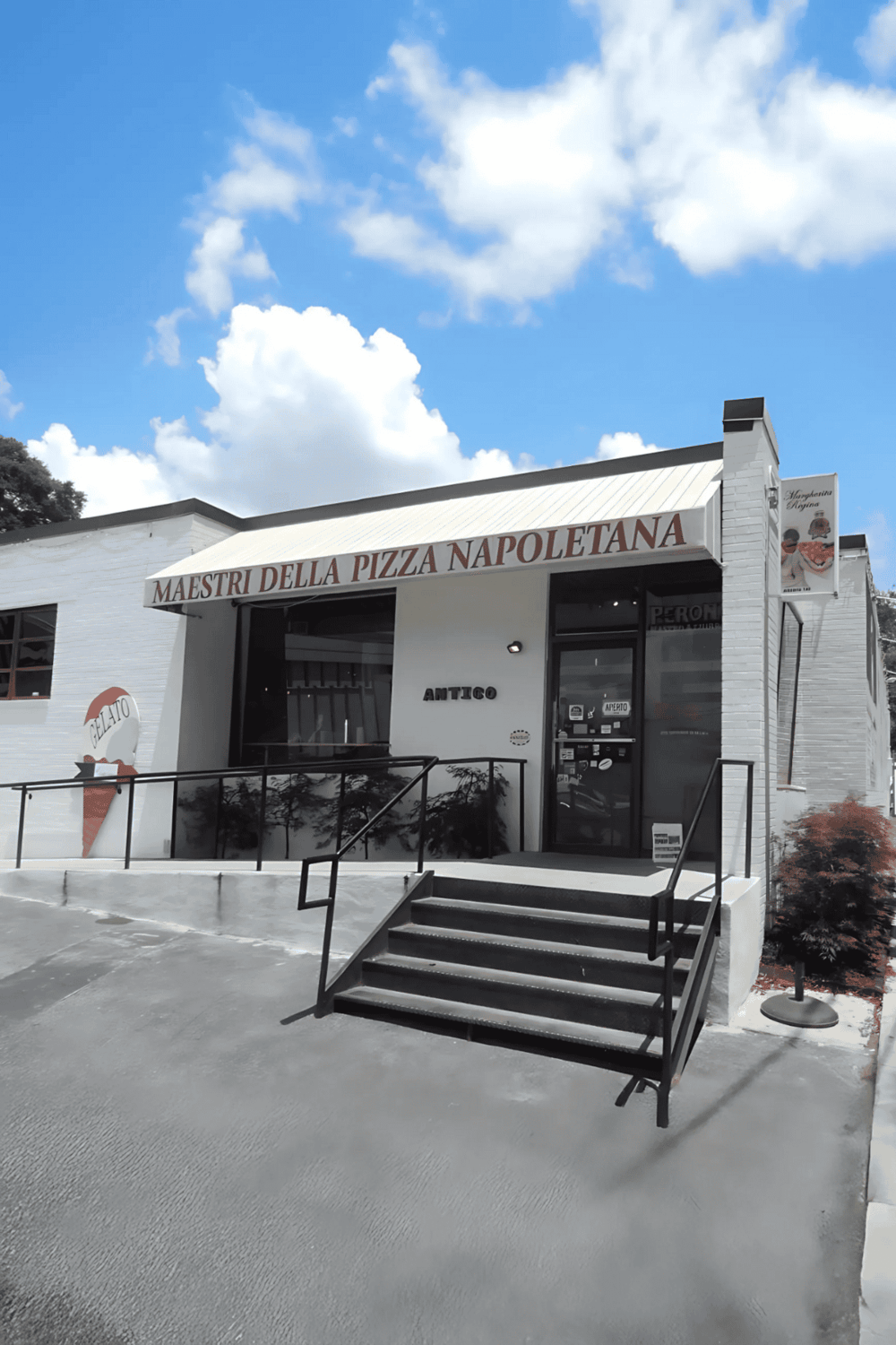 A pizza restaurant with a white exterior and black railing, featuring "Maestri Della Pizza Napoletana" signage.