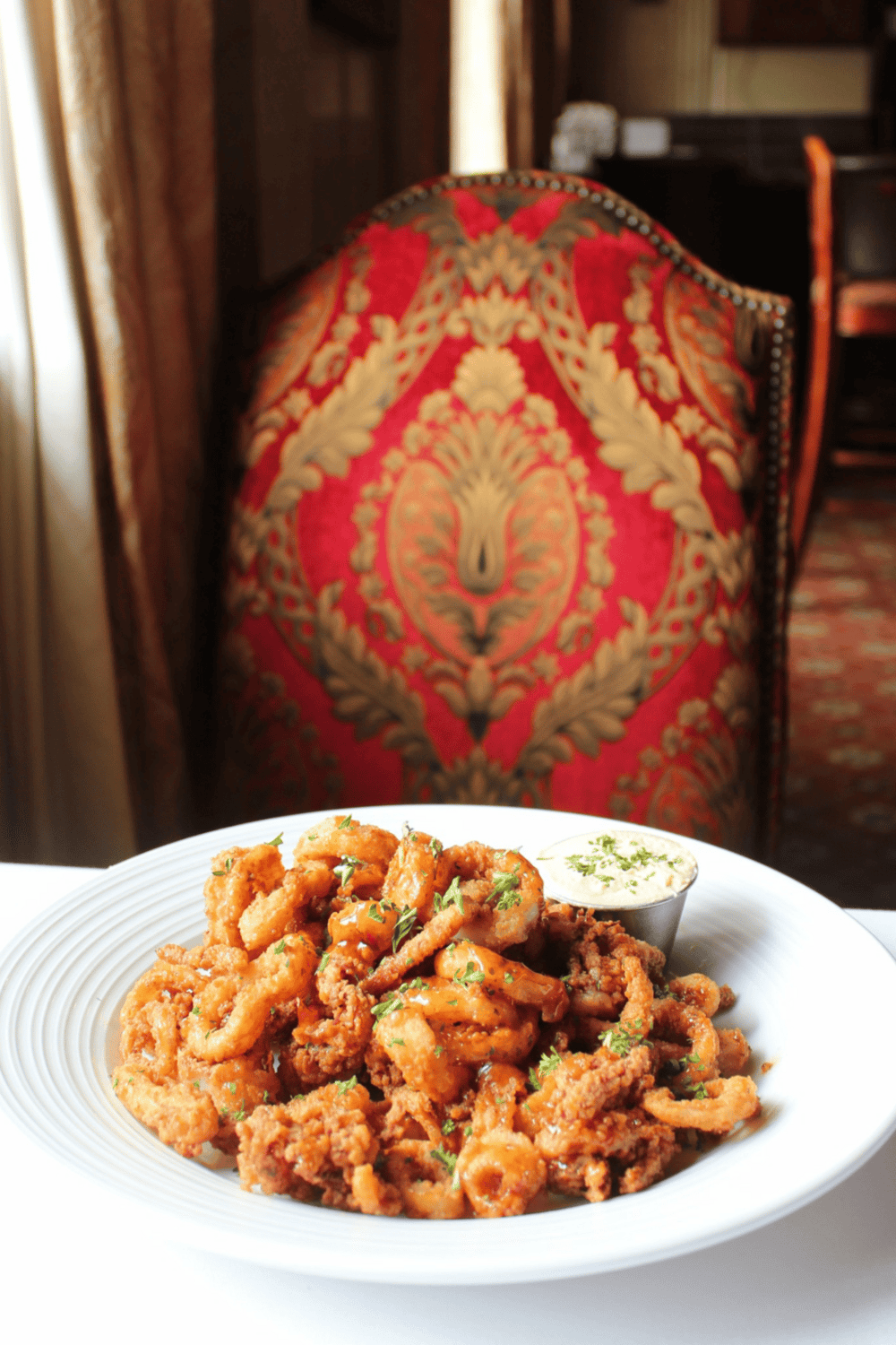 Crispy fried calamari with dipping sauce on a white plate, cozy restaurant setting, British cuisine dining experience.