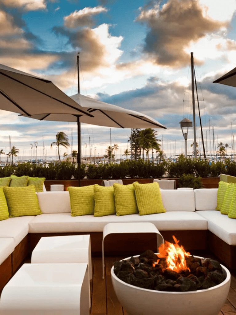 Relaxing outdoor lounge with fire pit near marina, perfect for seaside dining and sunset views.