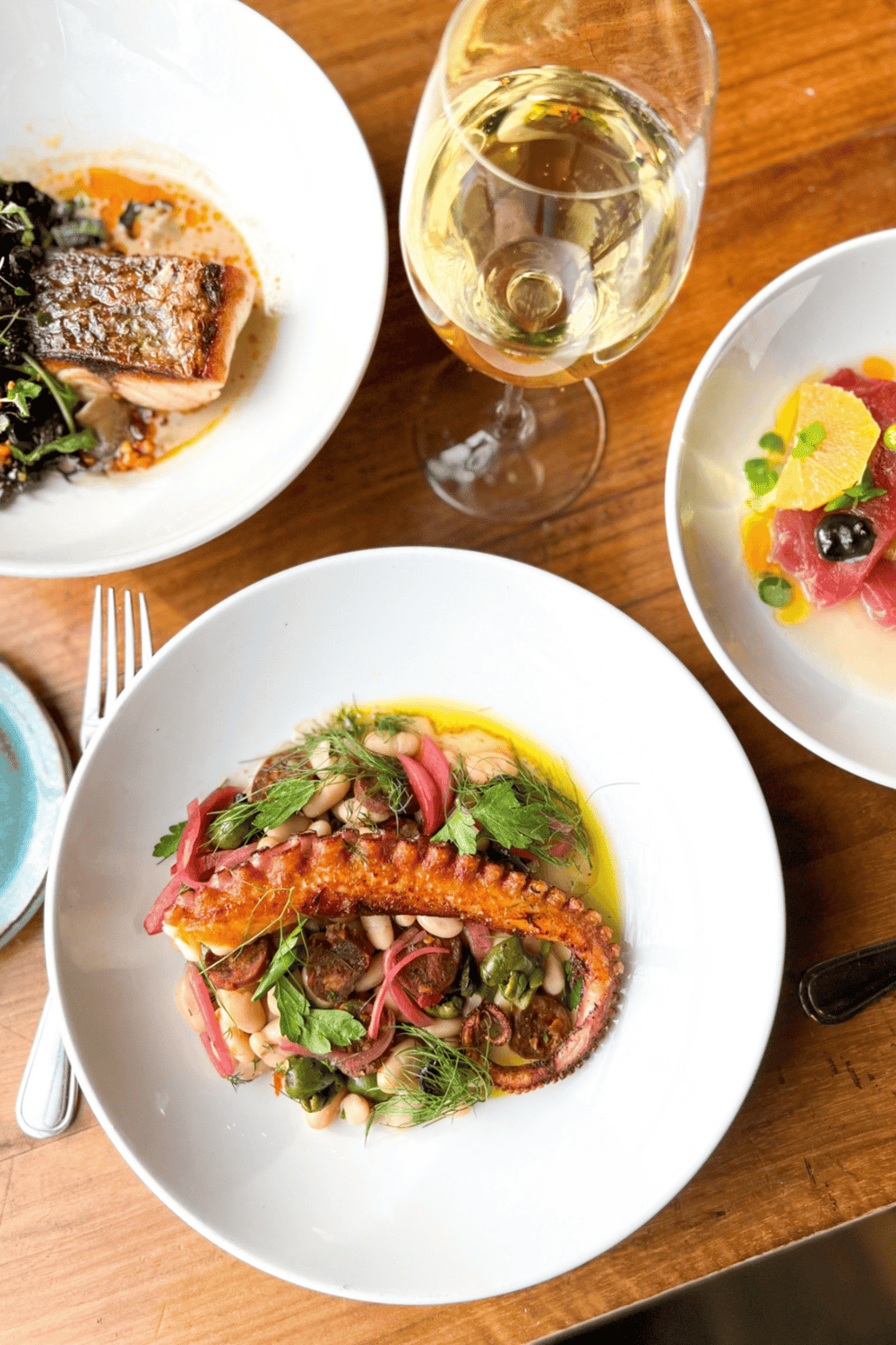 Premium seafood dish with grilled octopus, fresh herbs, and white beans on a white plate.