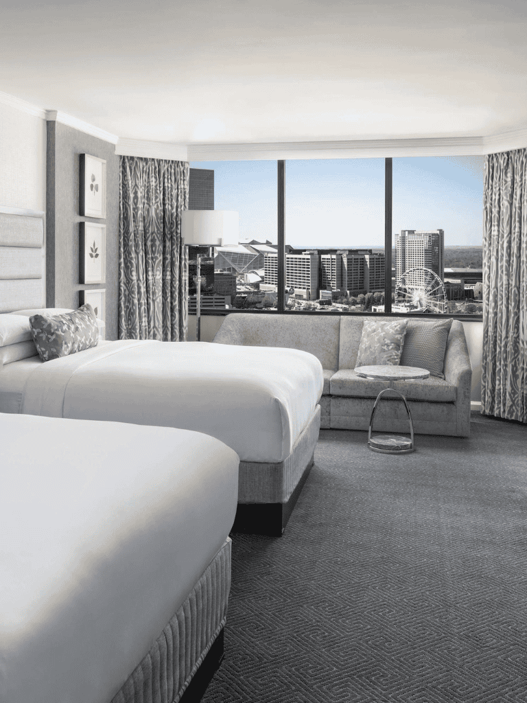 Luxury hotel room with city skyline view, modern decor, and spacious seating area.