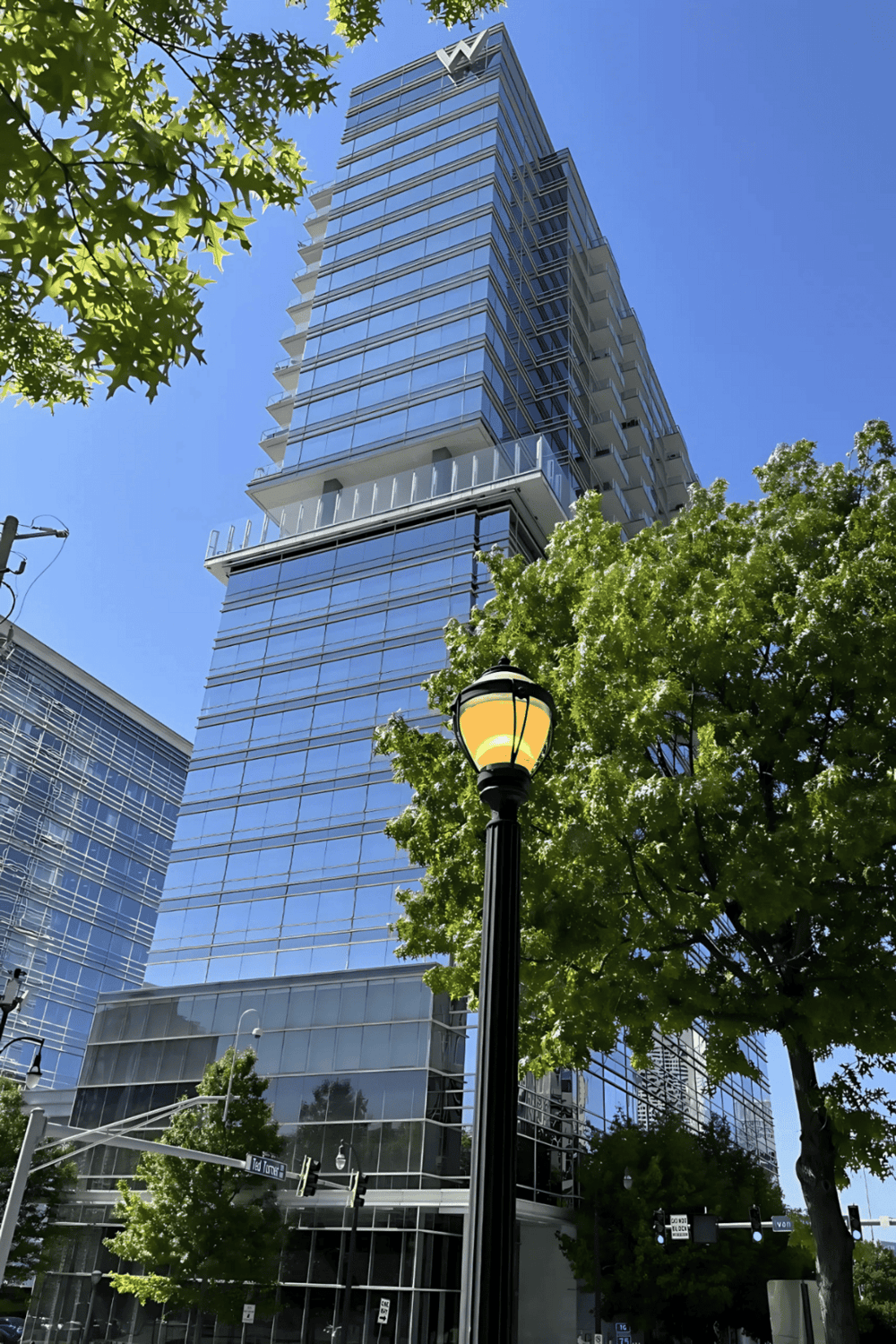 Contemporary glass skyscraper in downtown with green trees and street lamp, modern urban architecture.