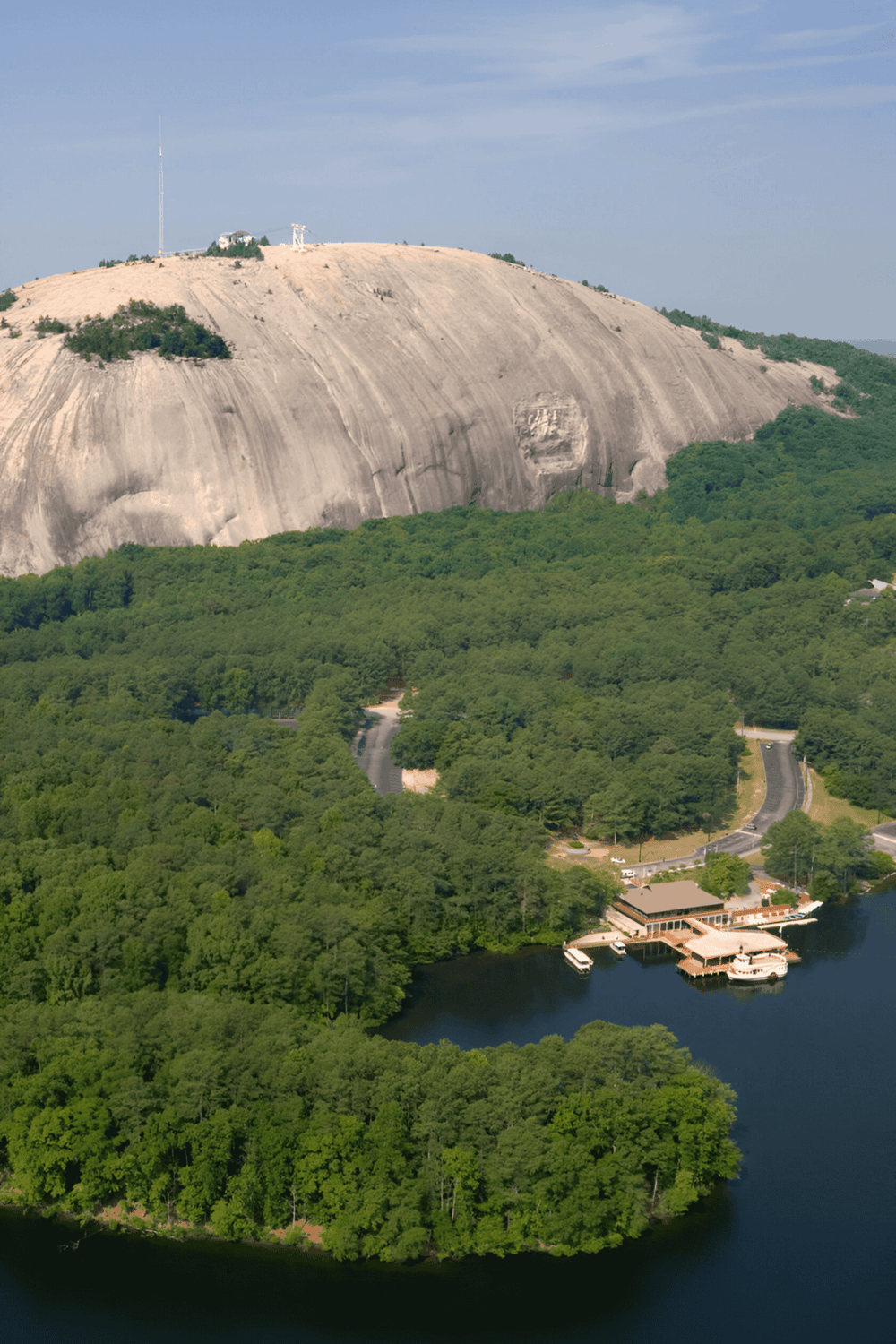 Ancient granite mountain with lush green trees and water body at the base, scenic natural landmark.