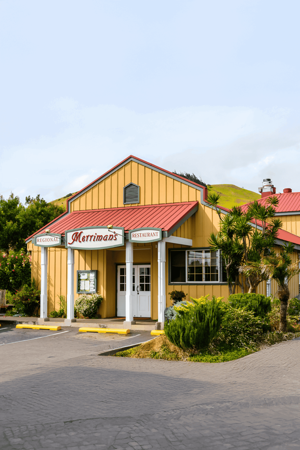 Bright yellow restaurant building with red roof and lush greenery, perfect for local dining and scenic travel stops.