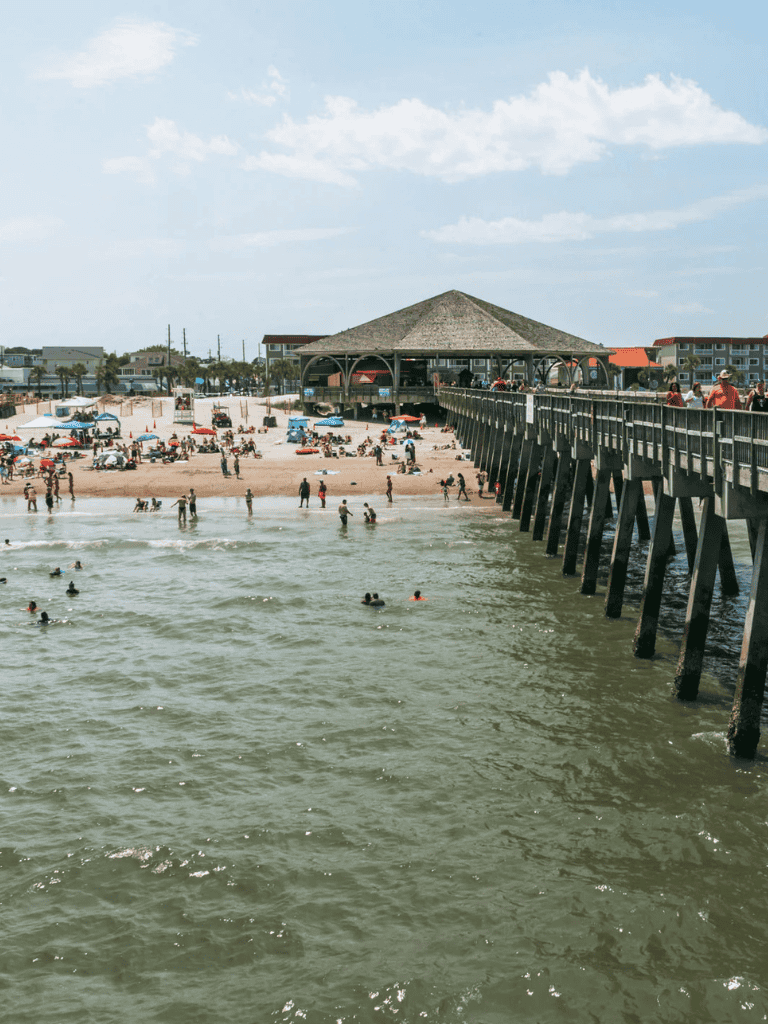 Beach pier with visitors and umbrellas, scenic coastal view for vacation destinations.
