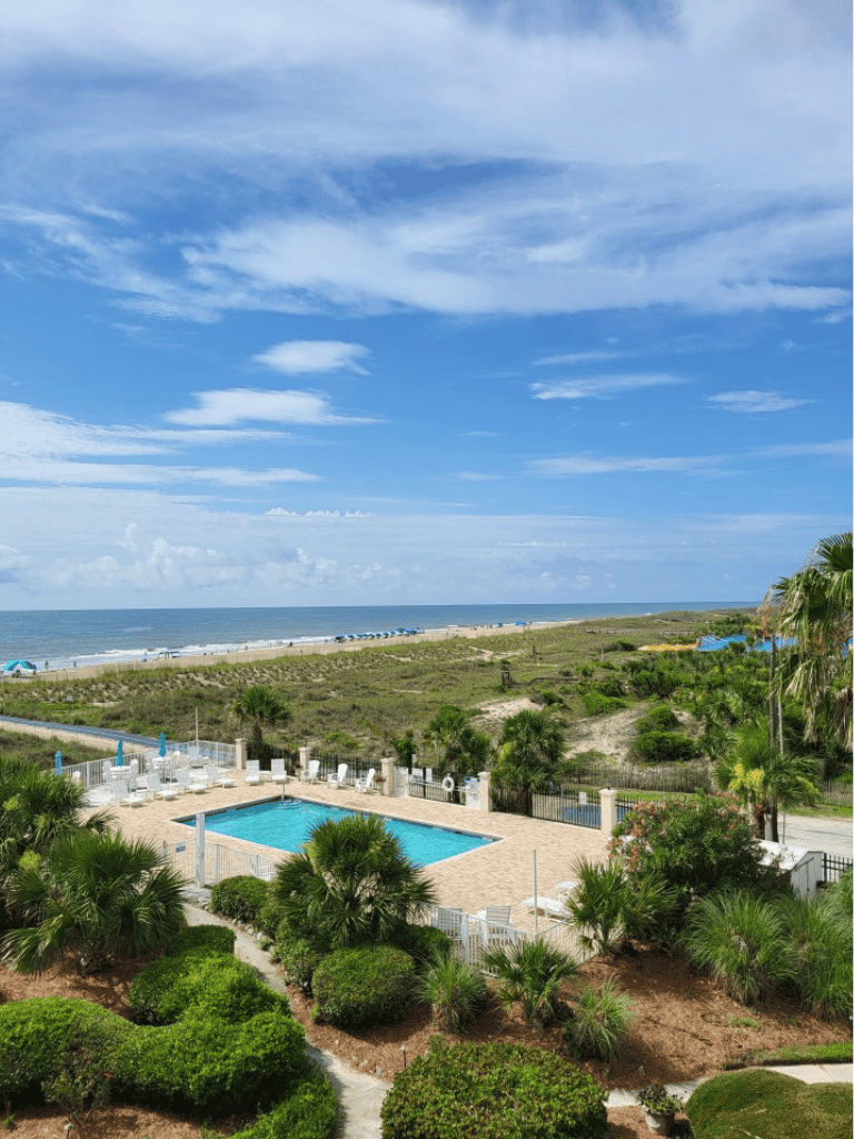 Aerial view of a private poolside area near the beach with lush greenery and scenic ocean view.