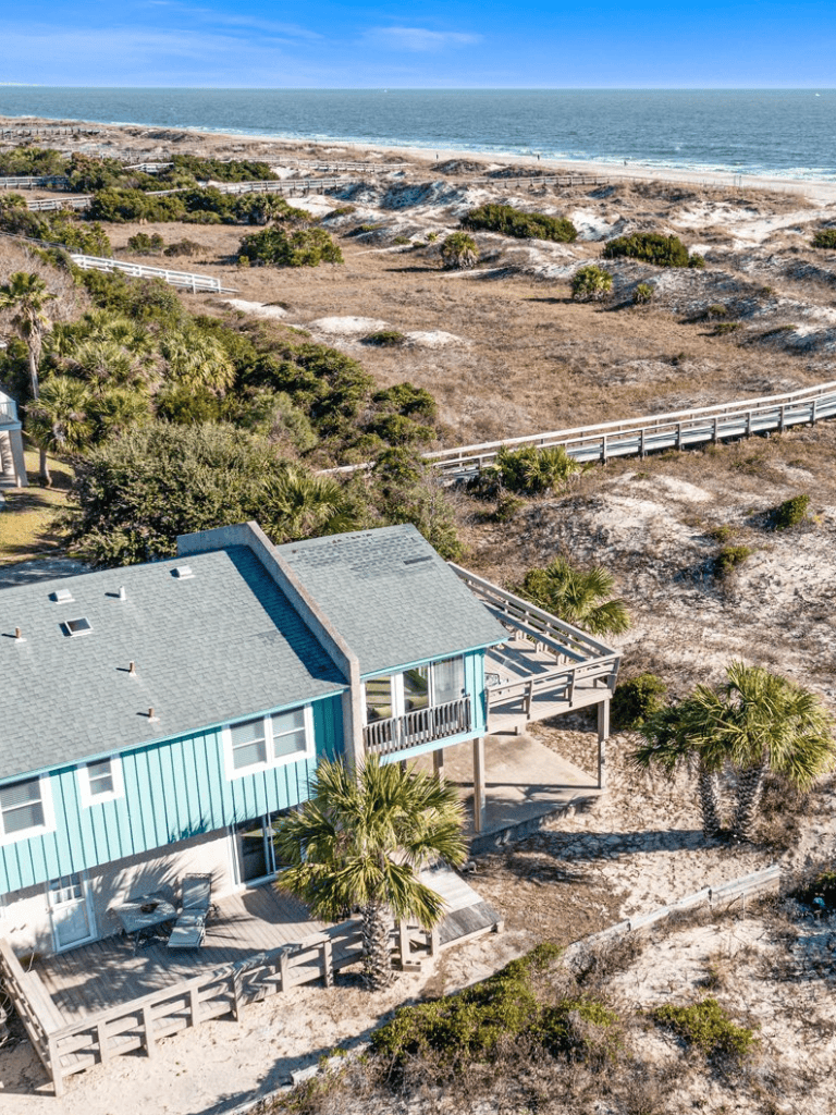 Spacious beach house with ocean view on sandy dunes, surrounded by palm trees and dunes.