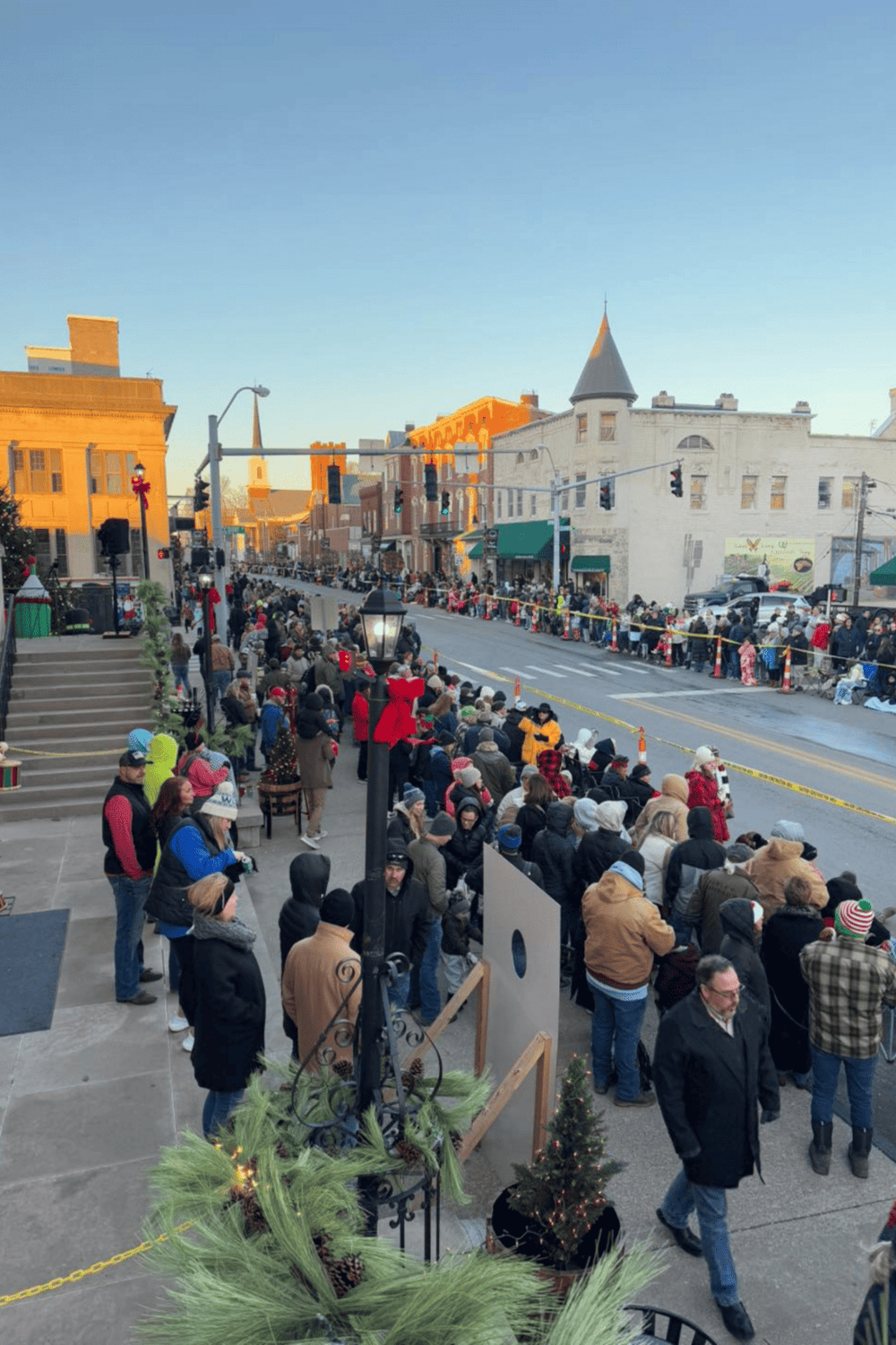 Crowd waiting in line for holiday event on a city street, festive atmosphere, Christmas decorations, urban neighborhood, evening light.
