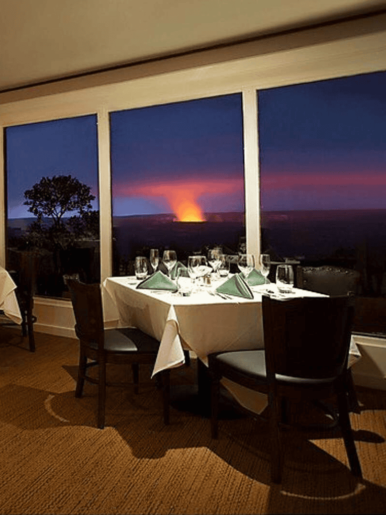 Vast sunset view through window from elegant dining area with table setting and green napkins.