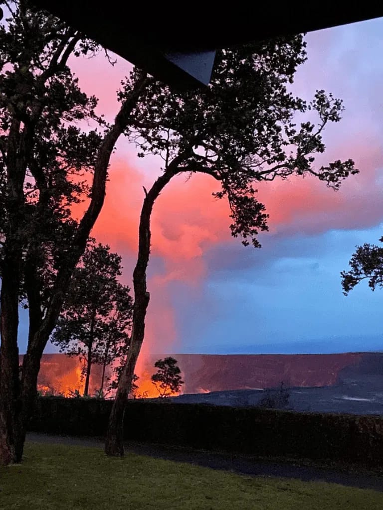 Volcanic eruption at sunset with smoke and trees silhouette, Hawaii scenic landscape.