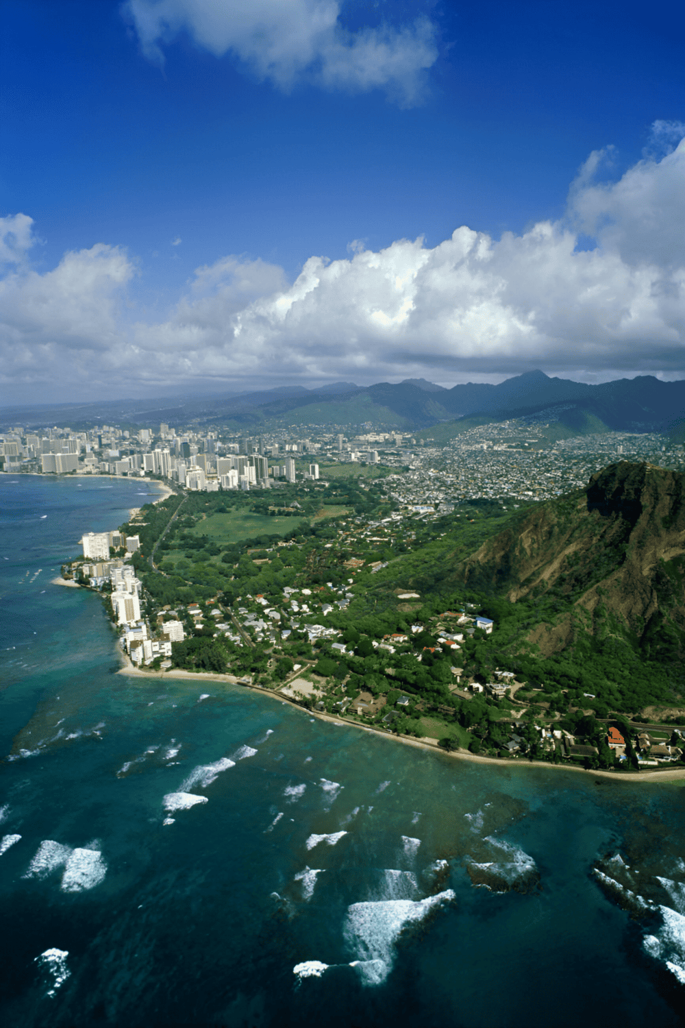 Aerial view of Honolulu skyline, lush mountains, and Pacific Ocean coastline in Hawaii.