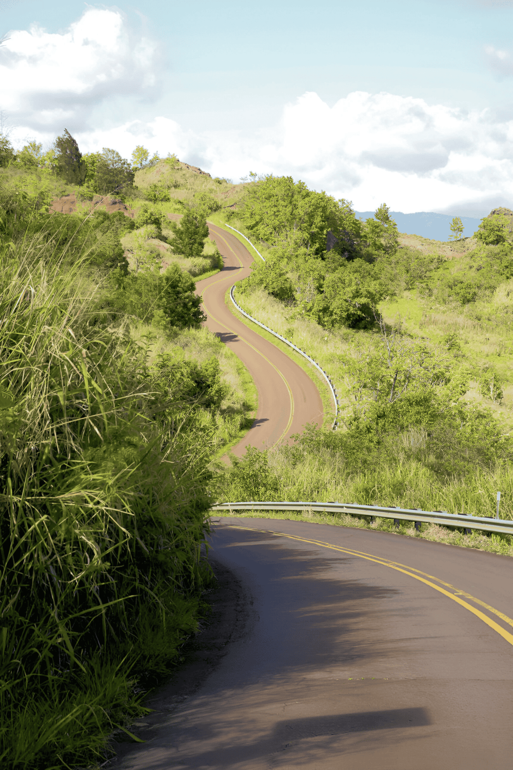 Winding mountain road surrounded by lush green landscape and blue sky, perfect for travel navigation and outdoor adventures.