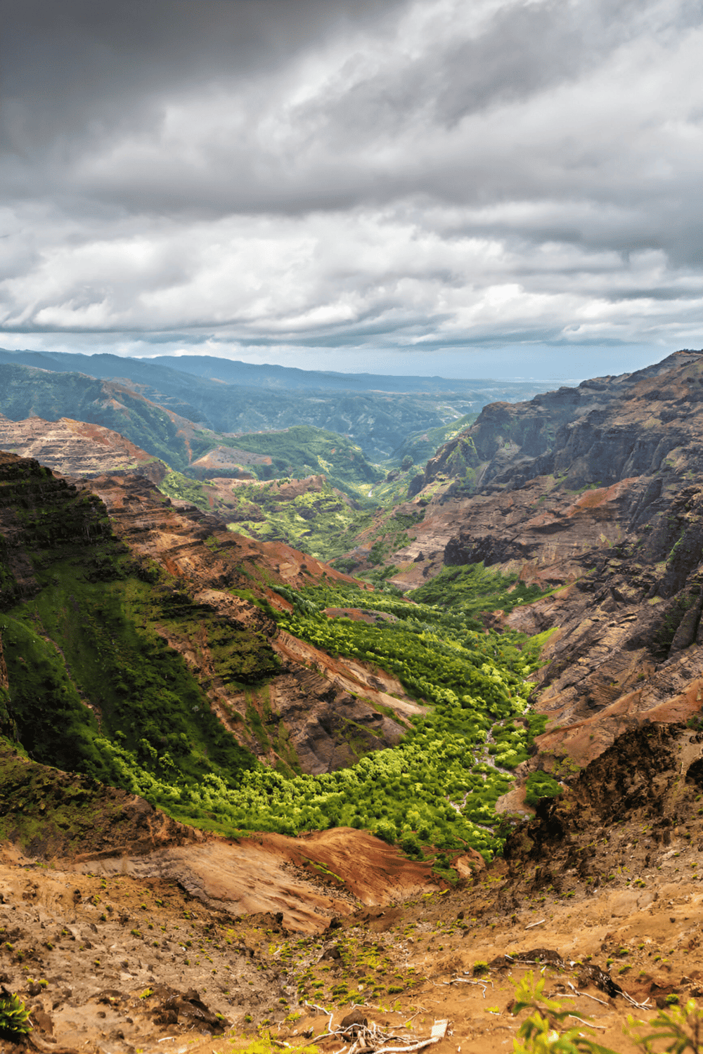 Vast canyon landscape with lush green valleys and dramatic hills under cloudy sky.